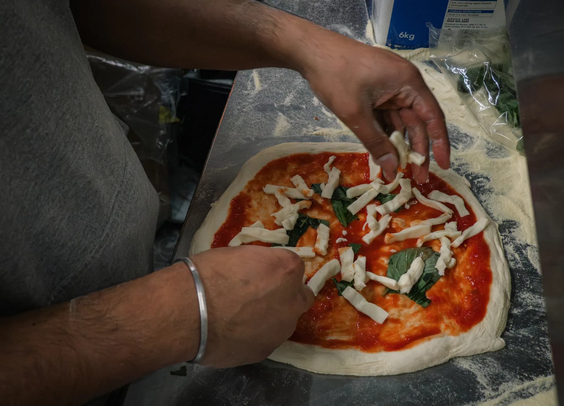 Fornoza sourdough pizza being hand-topped, fresh for service
